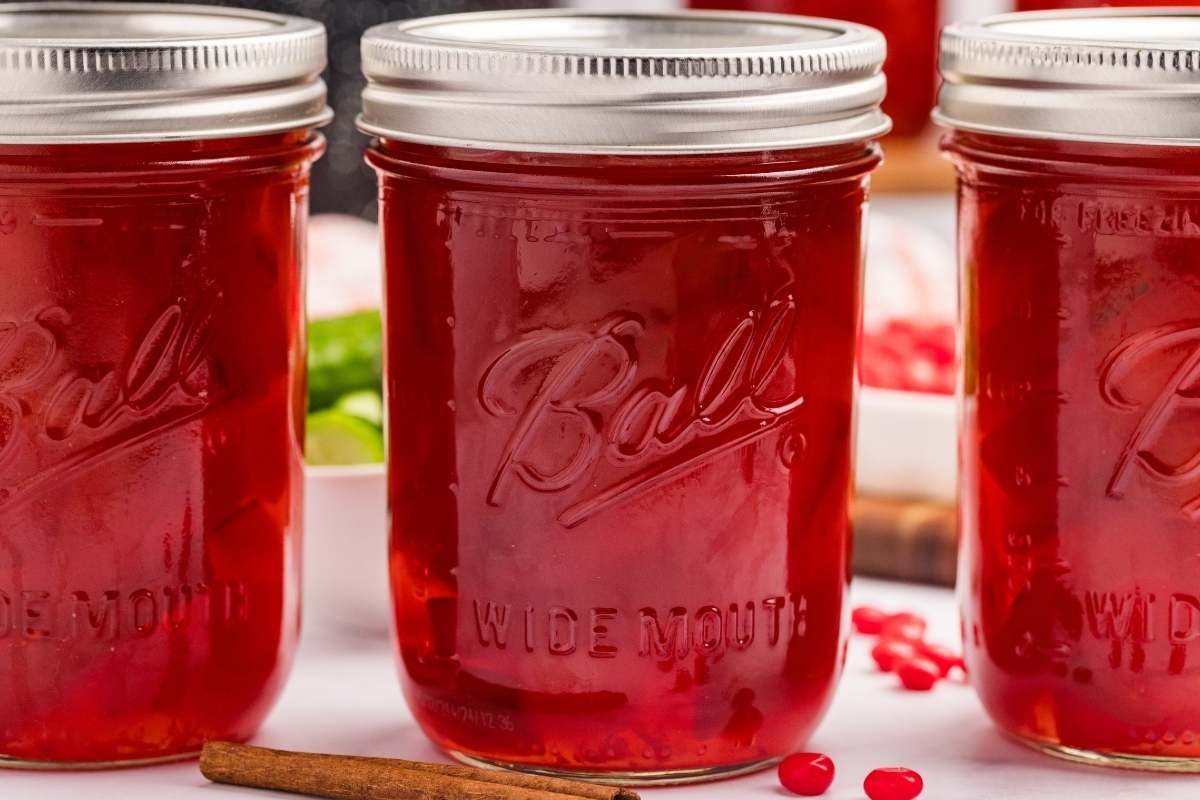 Three jars of red cinnamon pickles sealed in Ball canning jars.
