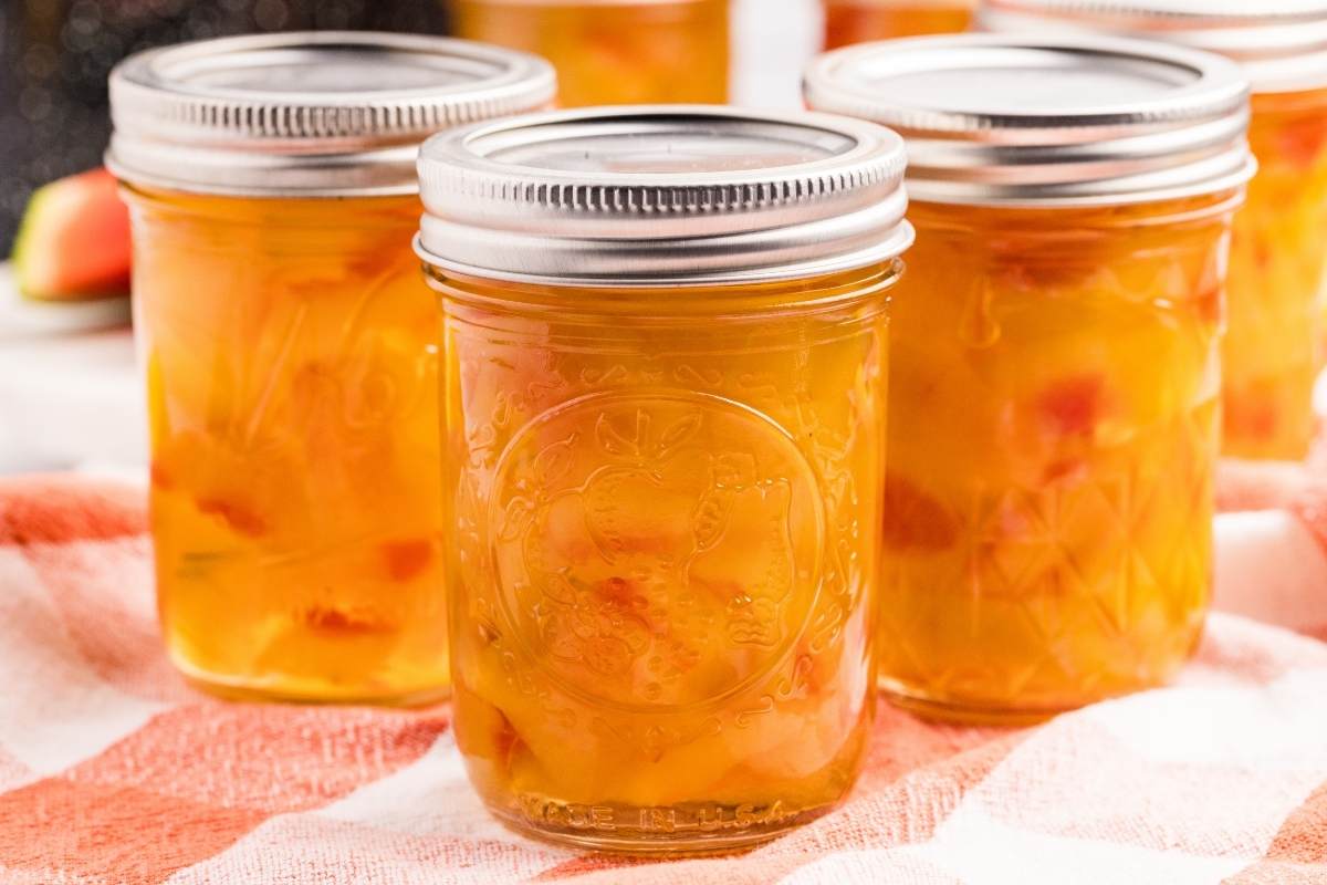 Multiple mason jars of watermelon rind pickles with metal lids on kitchen counter.