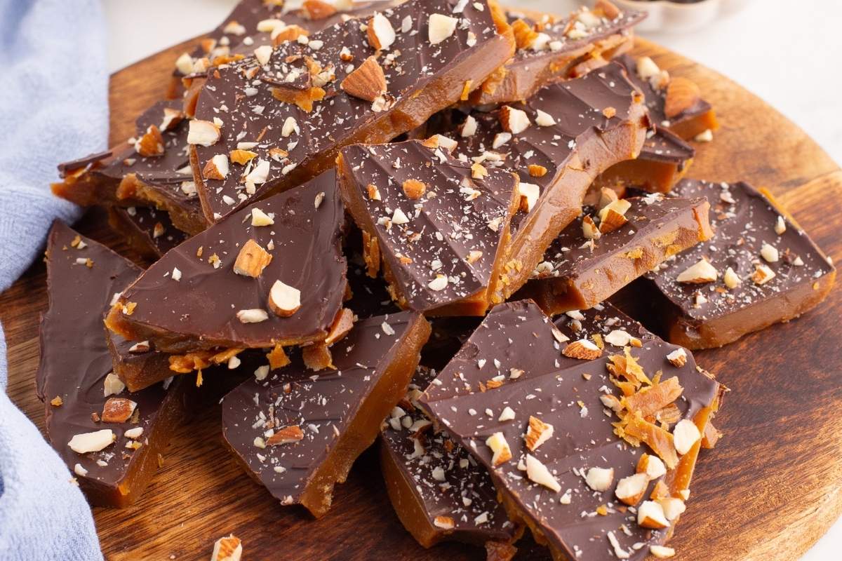 Pile of chocolate almond toffee pieces on a wooden board.