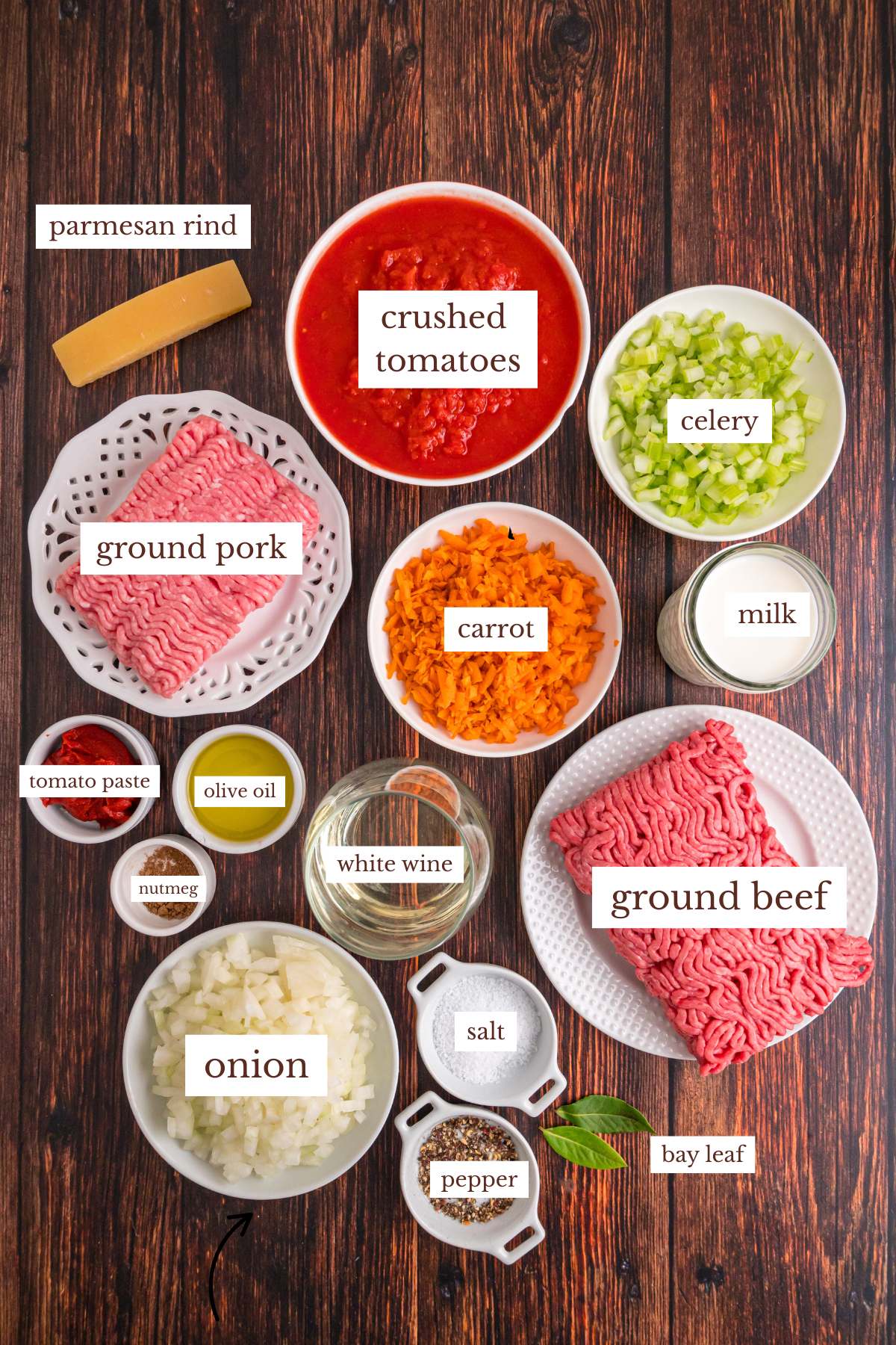 Ingredients for Bolognese sauce arranged on a wooden table.