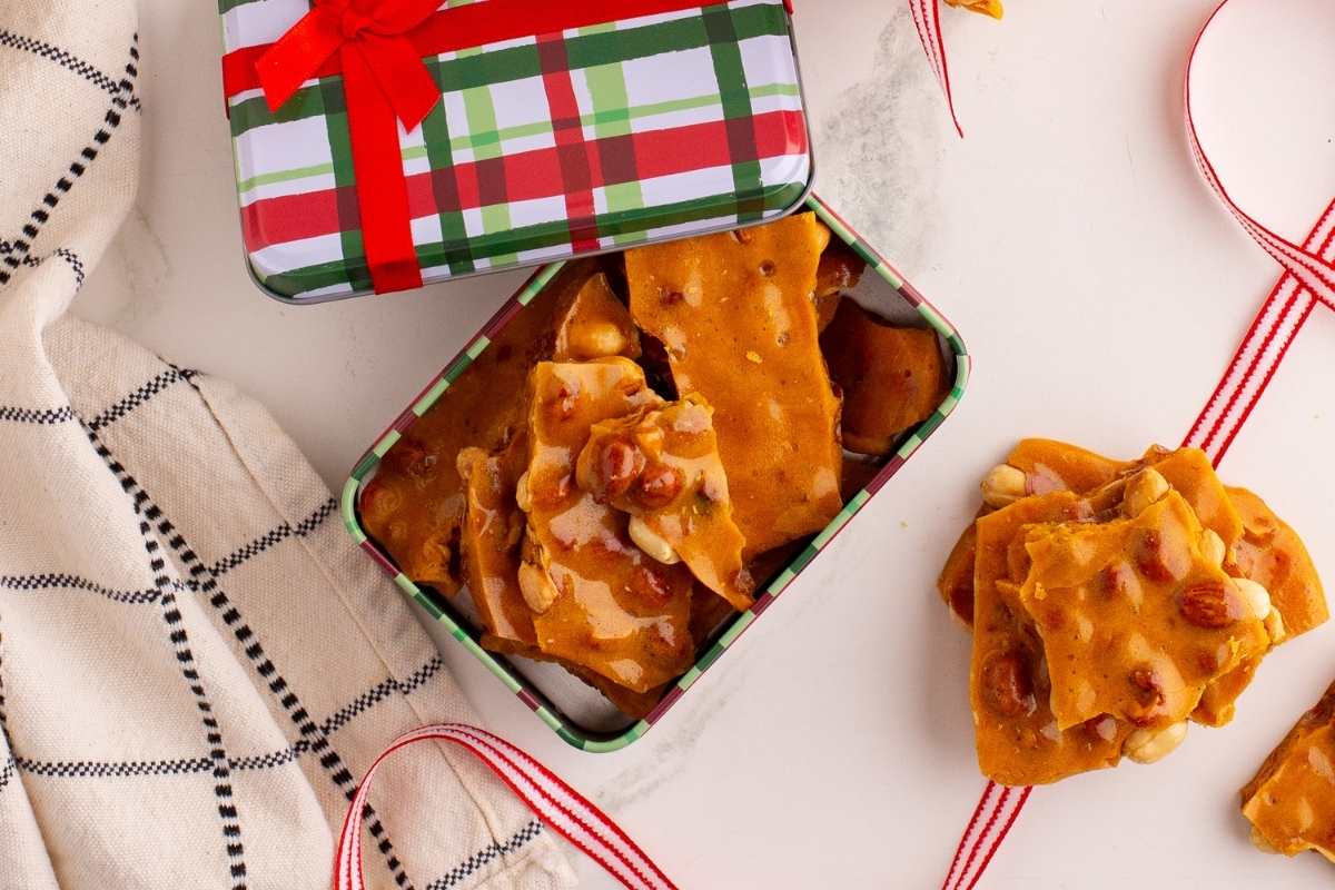 Broken peanut brittle pieces on parchment paper with a knife.