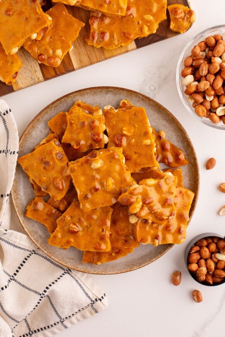 Plate of peanut brittle squares with peanuts on the side.