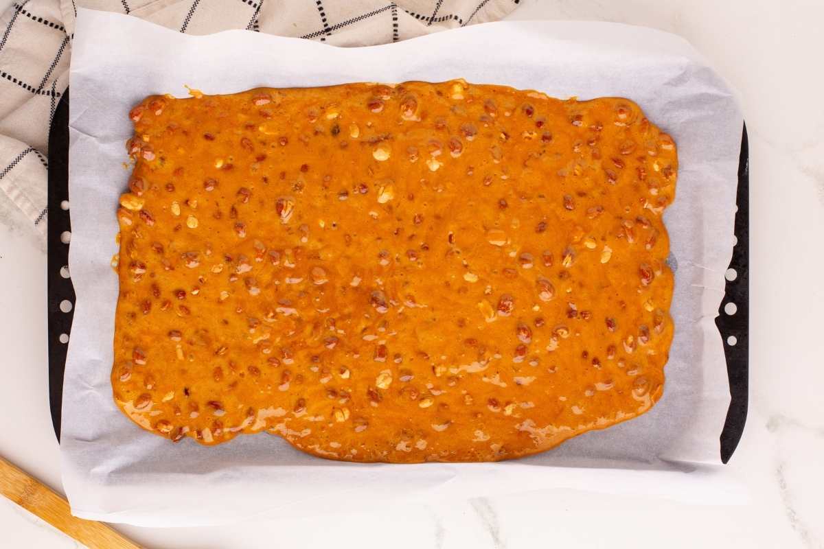 Freshly poured peanut brittle cooling on a parchment-lined baking sheet.
