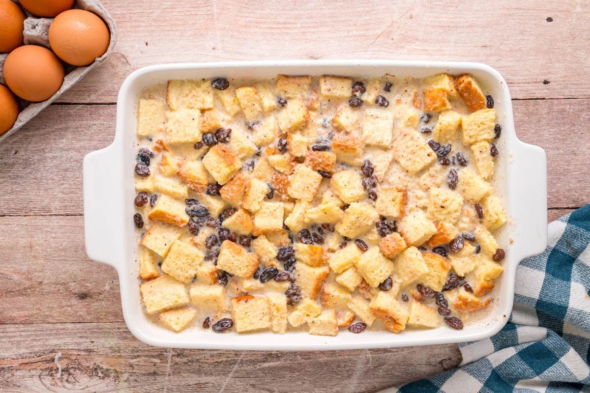 Unbaked bread pudding with custard poured over bread cubes and raisins.