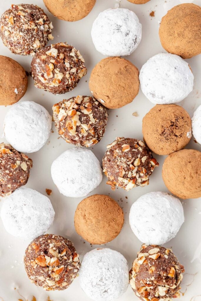 Mixed bourbon balls coated in cocoa, powdered sugar, and chopped pecans on a tray.