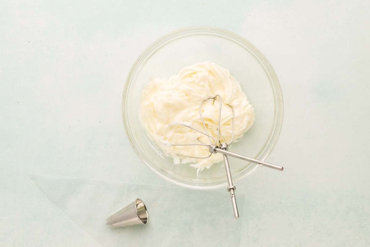 Bowl of lemon buttercream frosting with beaters and piping tip.