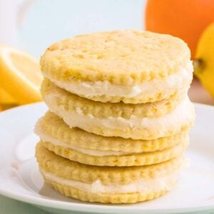 Stack of lemon shortbread sandwich cookies with lemons and oranges in background.