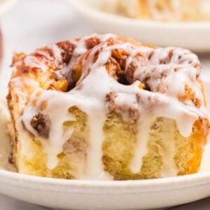 Peach cobbler cinnamon roll on a small plate with icing.