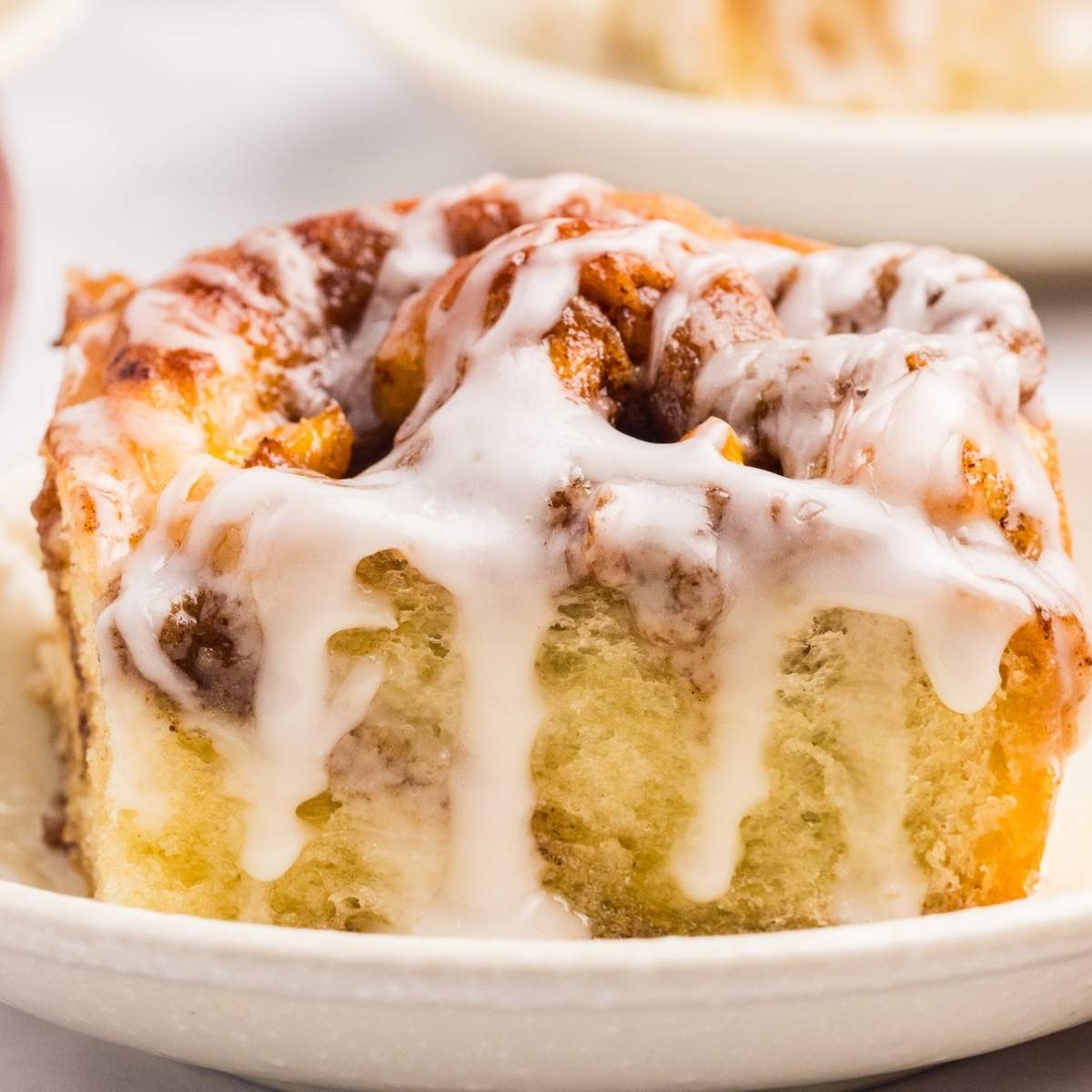 Peach cobbler cinnamon roll on a small plate with icing.