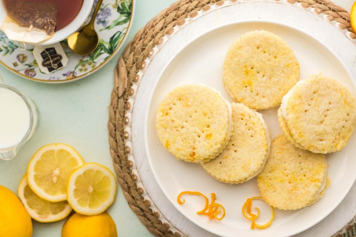 Round lemon shortbread cookies on a white plate with lemon slices.
