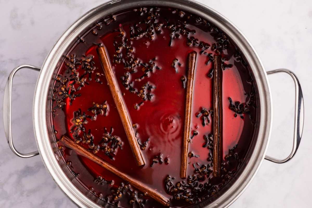 Spiced red syrup with cloves and cinnamon sticks in pot.