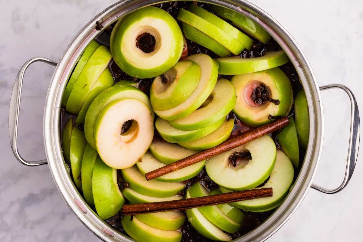 Apple rings simmering in red cinnamon syrup with spices.