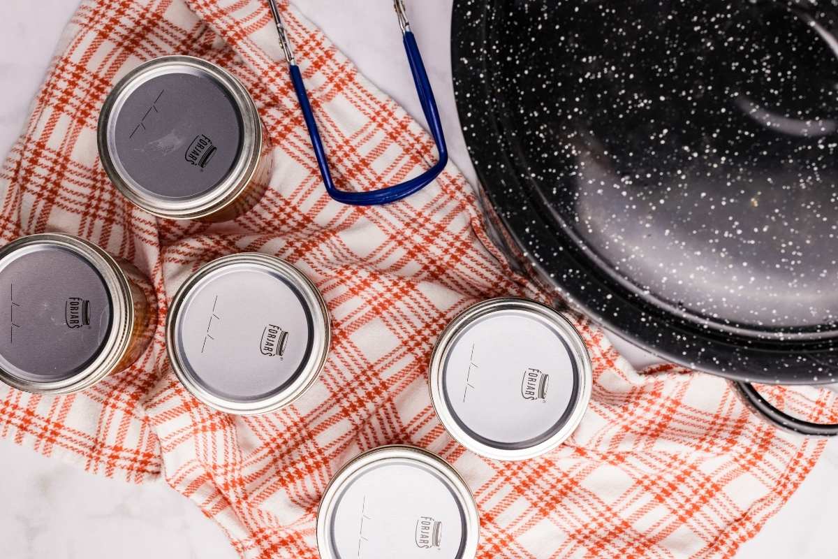 Canned jars cooling on a towel next to a canning pot.