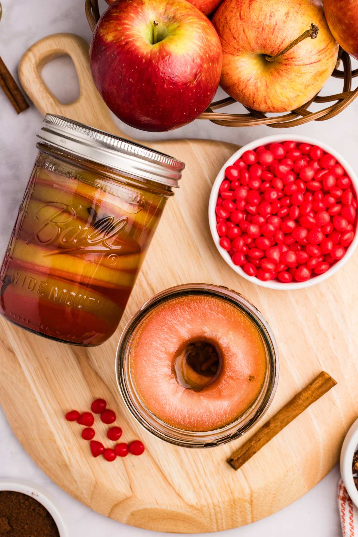 Jar of apple rings with apples and red candy pieces nearby.