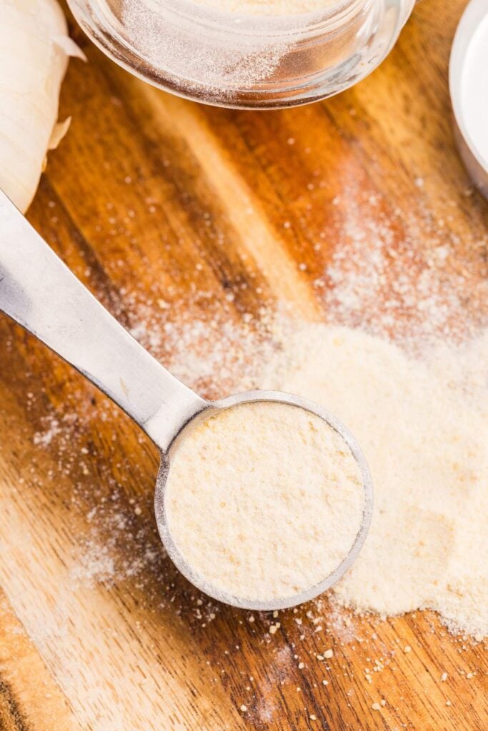 Jar of garlic powder on wooden board.