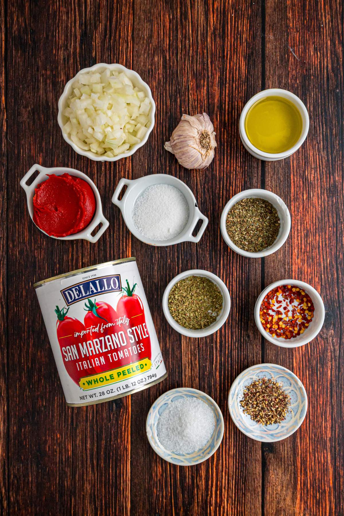 Canned tomatoes, chopped onions, garlic, and spices arranged on a wooden table.