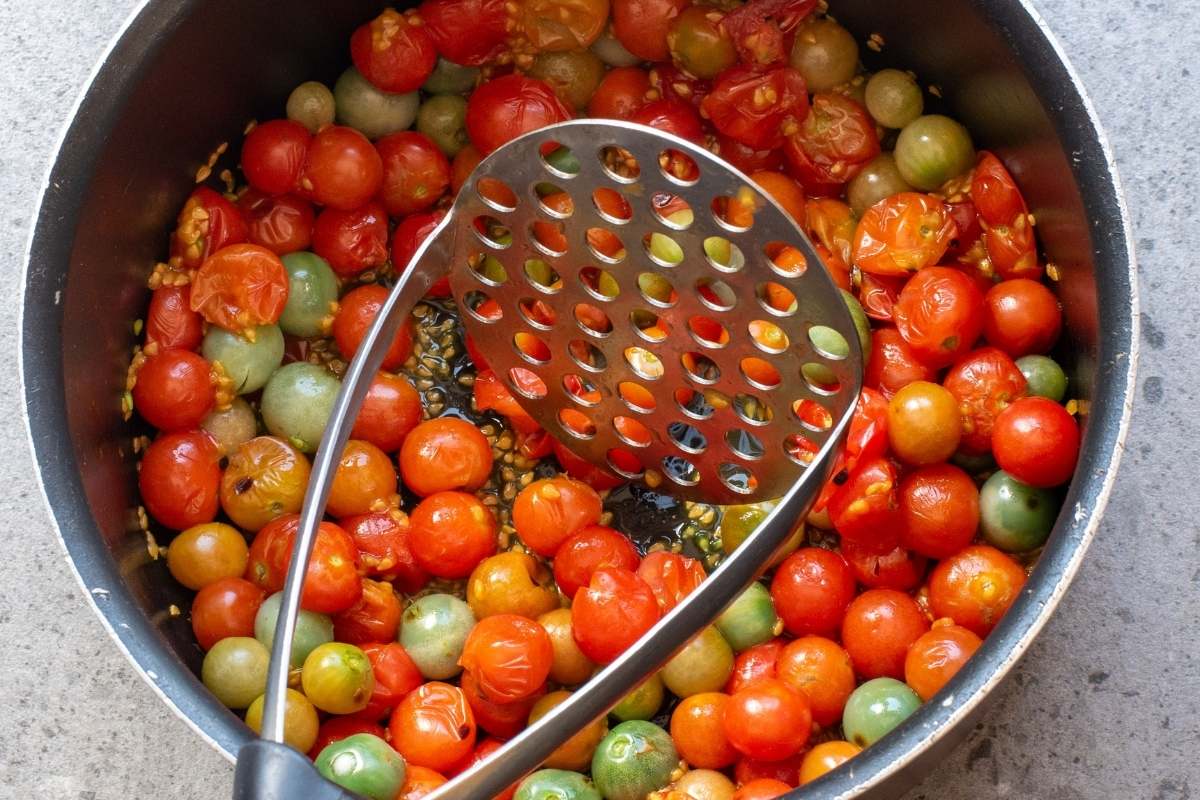 Whole tomatoes in pot with a masher.