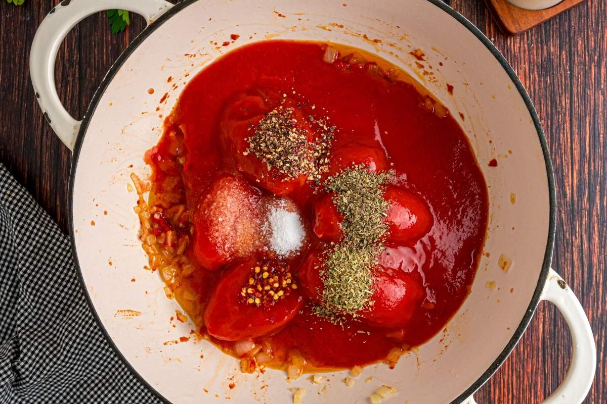 Whole canned tomatoes and dried herbs added to the pot with onions.