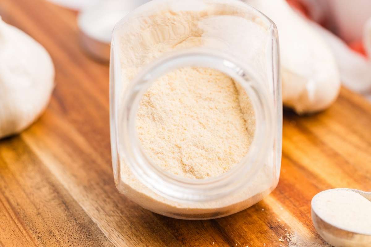 Spoon and jar of garlic powder on wooden board.