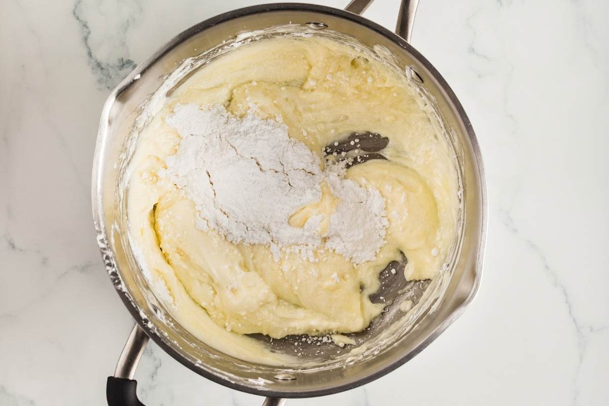 Cream cheese mixture in a saucepan with powdered sugar being stirred in.