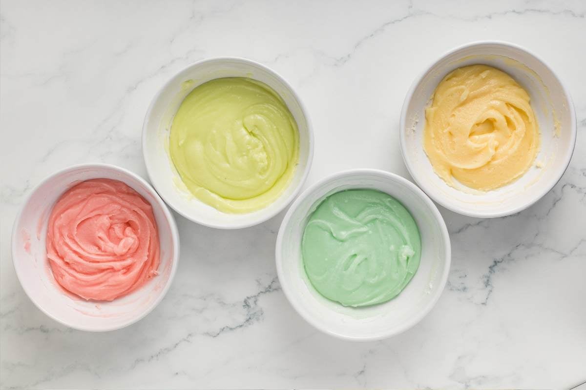 Four bowls of tinted mint mixture in pink, green, yellow, and white.
