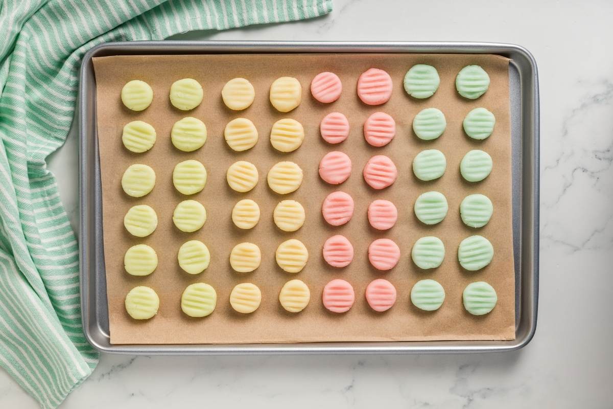 Pink, green, and yellow cream cheese mints arranged on a parchment-lined baking sheet.