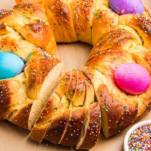 Sliced Italian Easter bread ring with colorful dyed eggs and rainbow sprinkles.