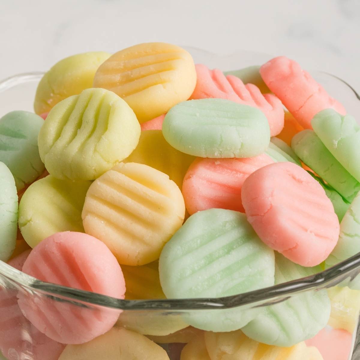 Pink, green, and yellow cream cheese mints in a scalloped glass dish.