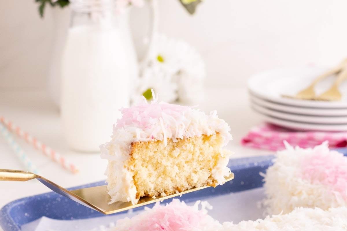 A slice of coconut cake with pink and white frosting on a gold server.