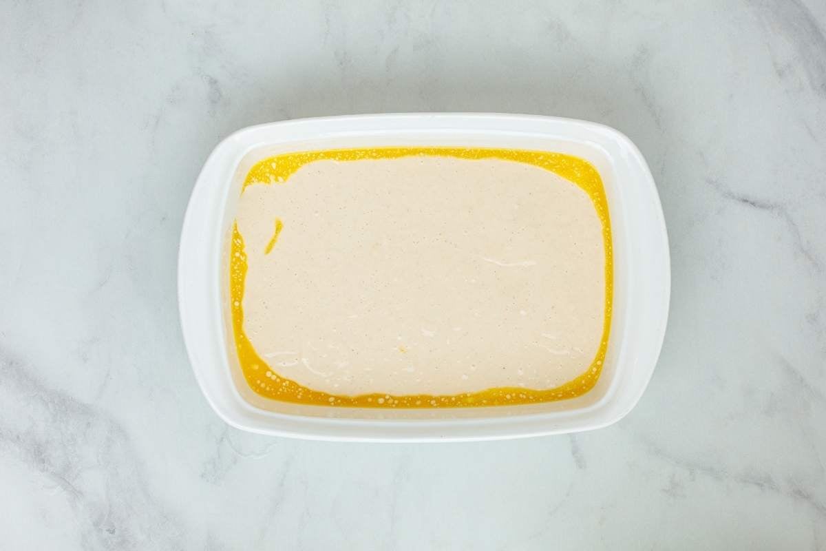 Smooth wet batter poured over melted butter inside a white rectangular baking dish.