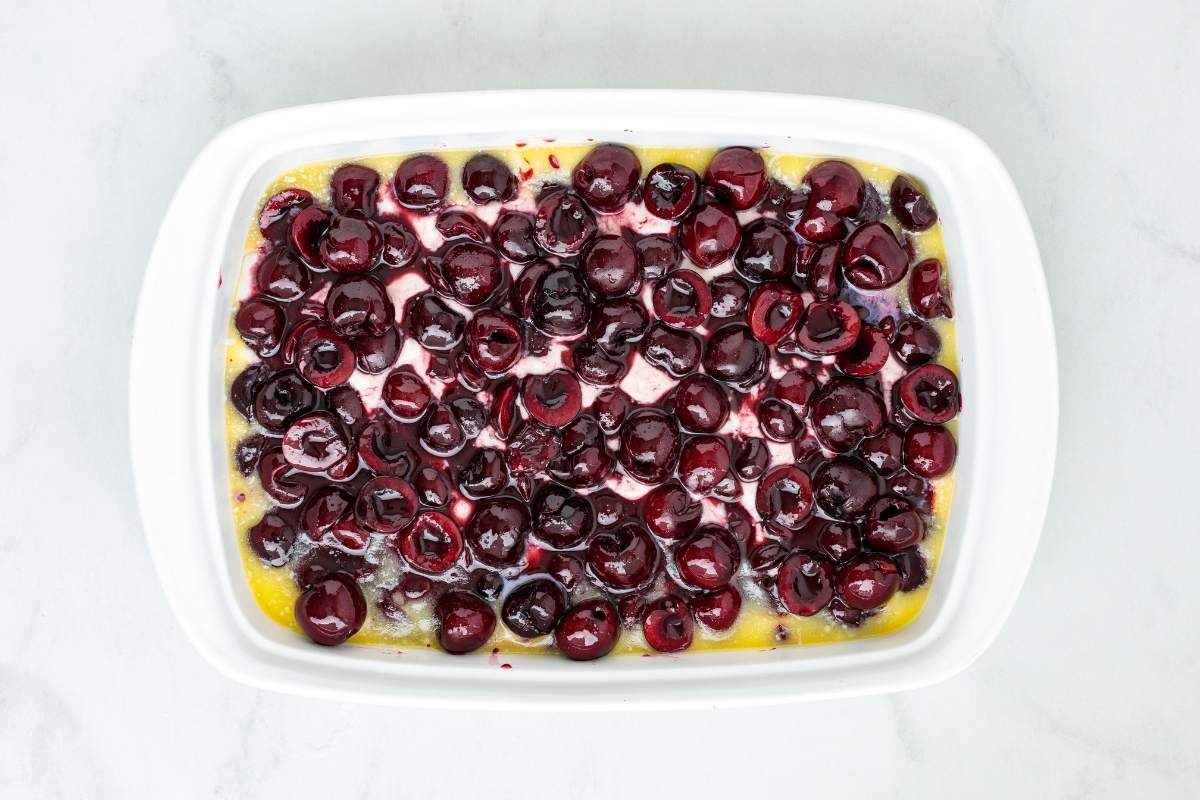 Pitted cherries layered over wet batter in a white baking dish.