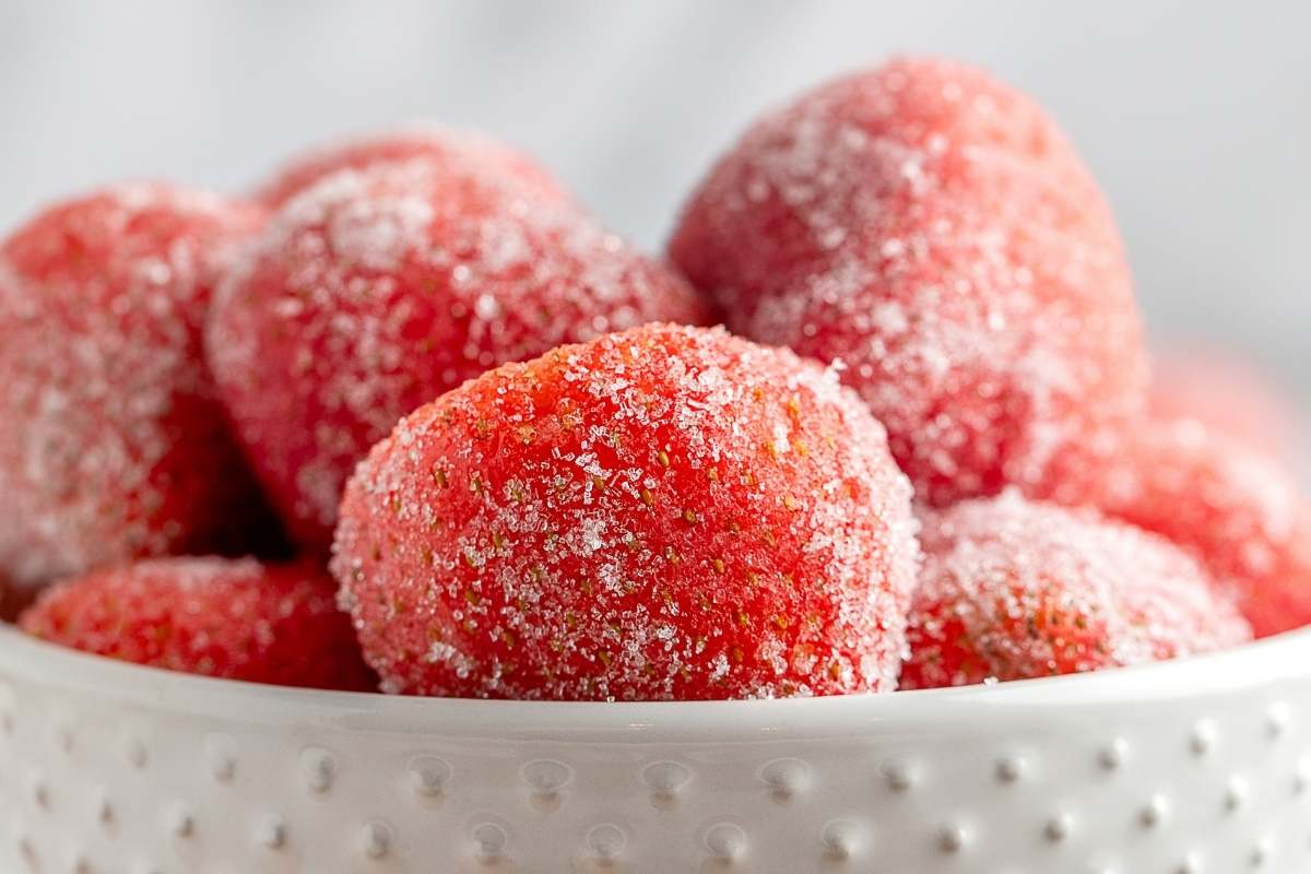 Sugar-coated strawberries piled in a small white bowl.