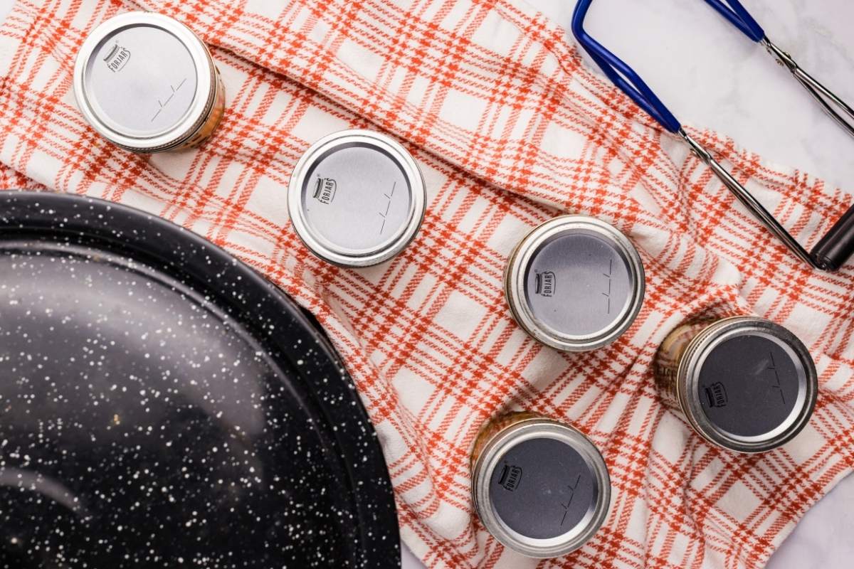 Sealed jars cooling on a plaid towel next to a water bath canner.