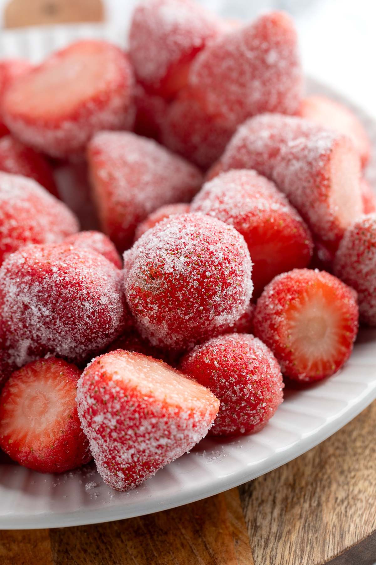 Sugar-coated strawberries piled on a white plate on a wooden surface.