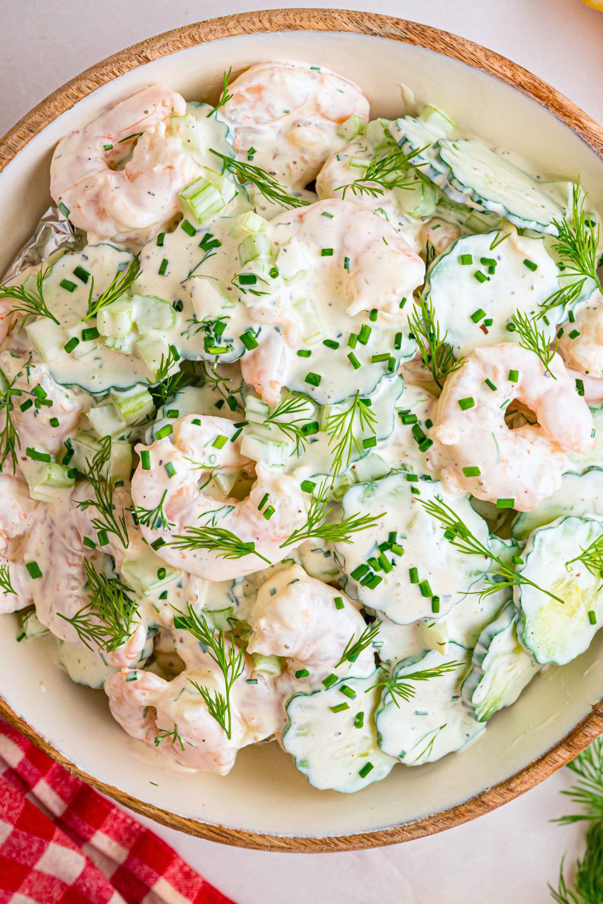 Close up of creamy shrimp and sliced cucumber salad in a wooden bowl.