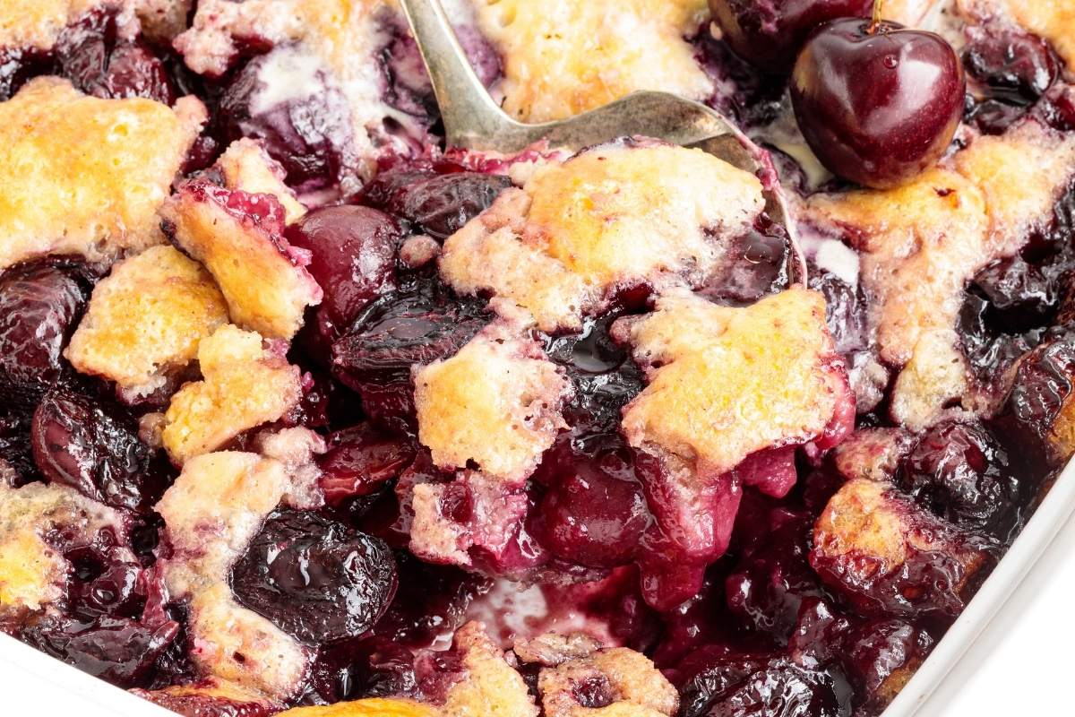 A close up of baked cherry cobbler being scooped with a silver spoon.