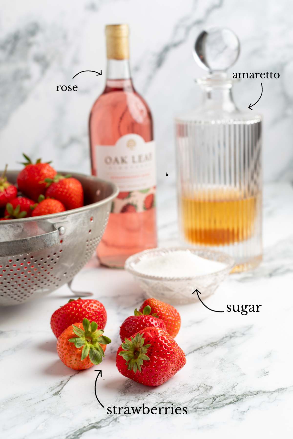 Labeled ingredients including strawberries, rosé, amaretto, and sugar on marble.