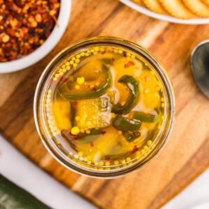 Open jar of candied pineapple and jalapeños in golden syrup viewed from above.