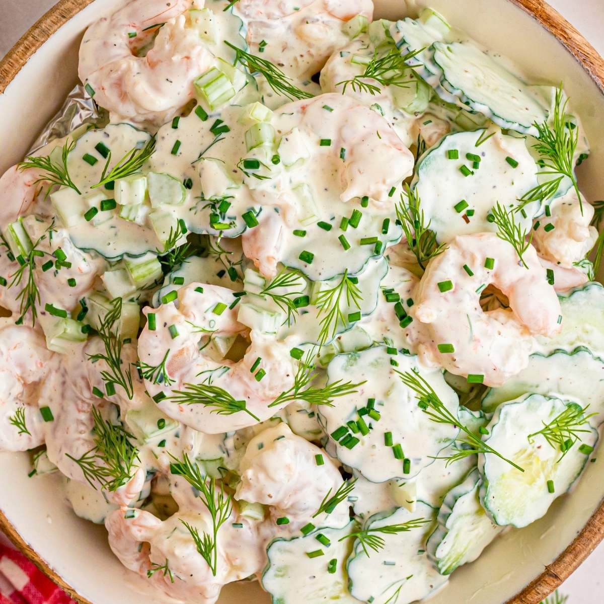Close up view of creamy shrimp and cucumber salad garnished with chopped herbs.