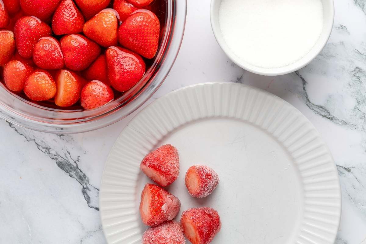 Soaked strawberries in a glass bowl next to a plate and sugar dish.