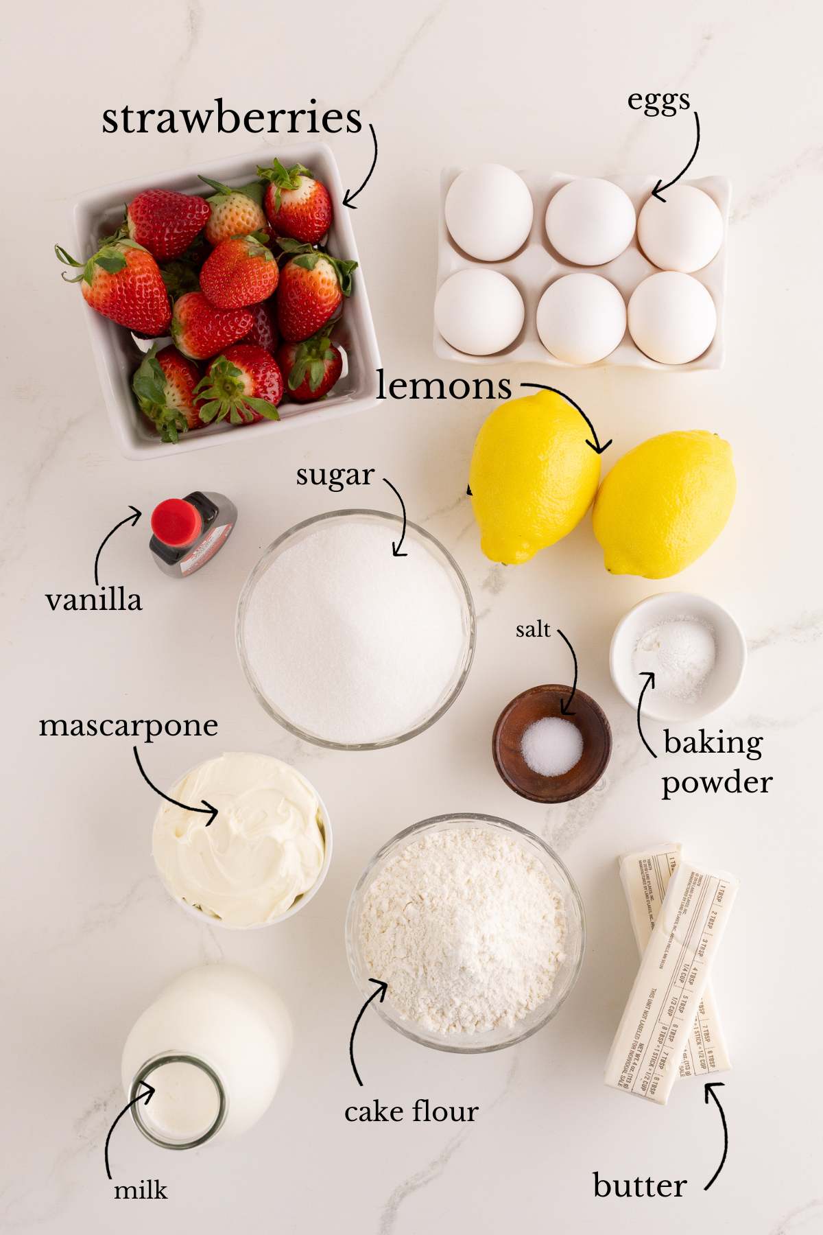 Ingredients laid out on a counter including strawberries, lemons, eggs, and flour.