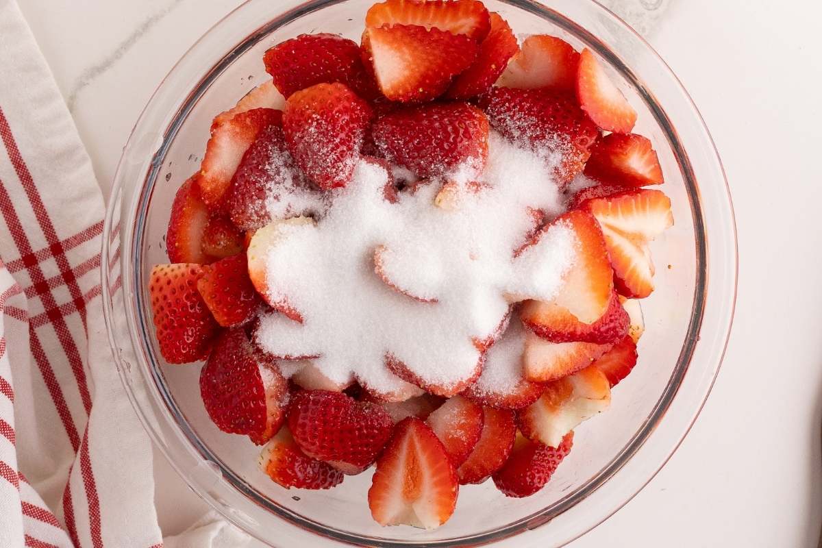 Sliced strawberries tossed with sugar in a glass bowl.