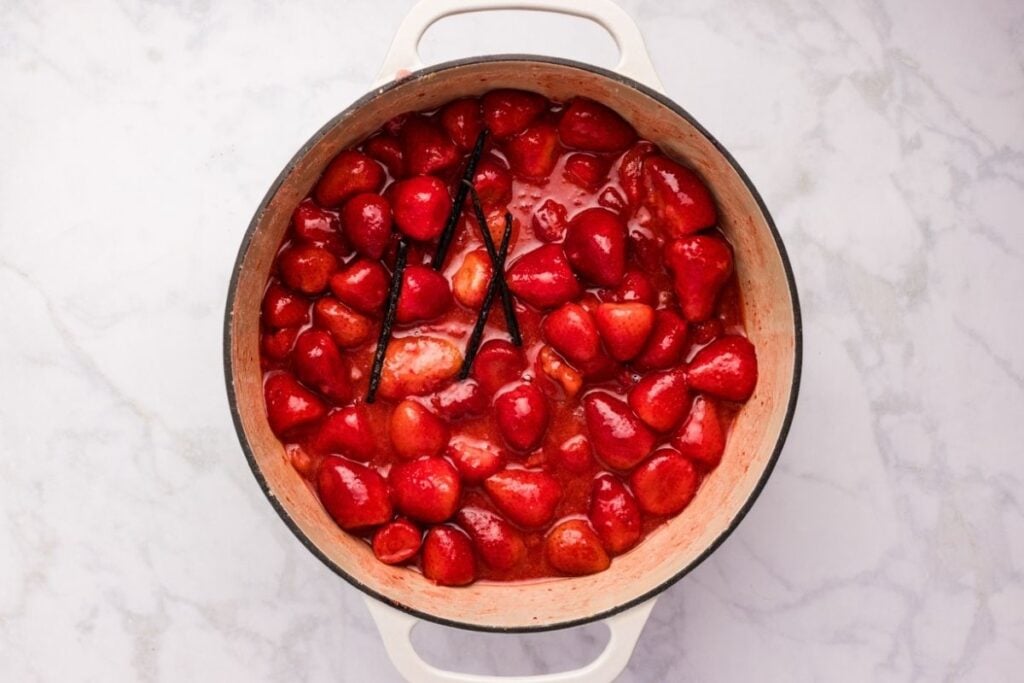 Strawberries simmering with vanilla beans in a pot of red liquid.