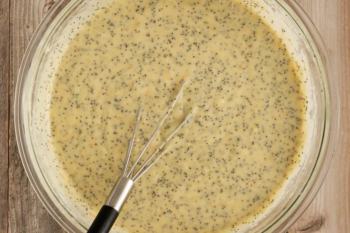 Orange poppyseed cake batter in a glass bowl with a whisk.