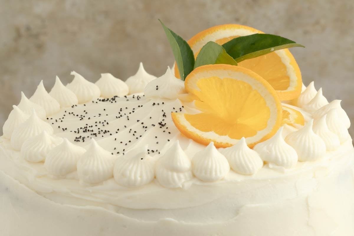 Decorated cake with piped frosting, orange slices, and poppy seeds.
