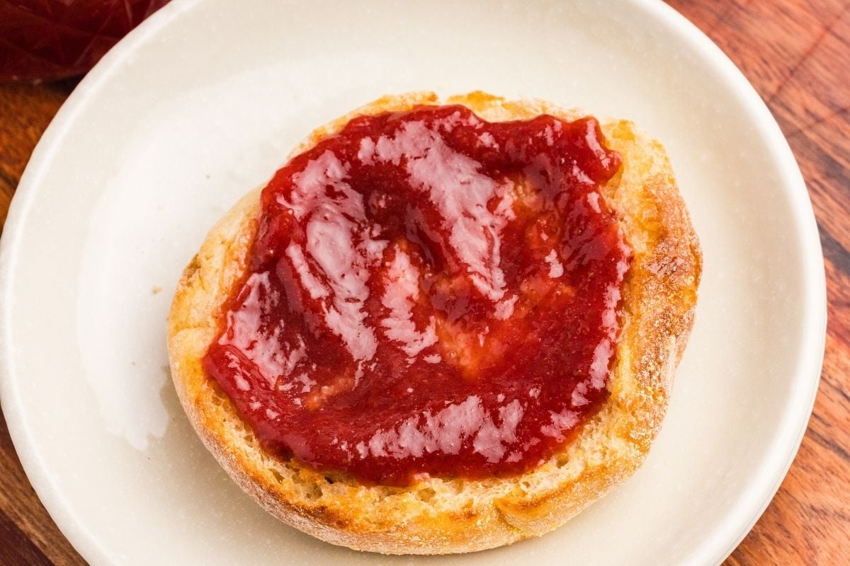 Strawberry butter spread on a toasted English muffin on a white plate.