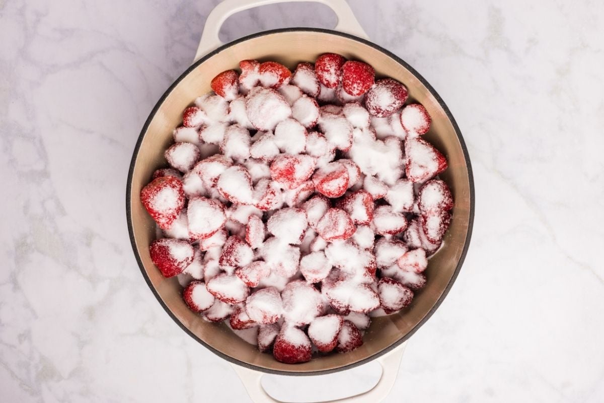Sliced strawberries mixed with sugar in a large pot seen from above.