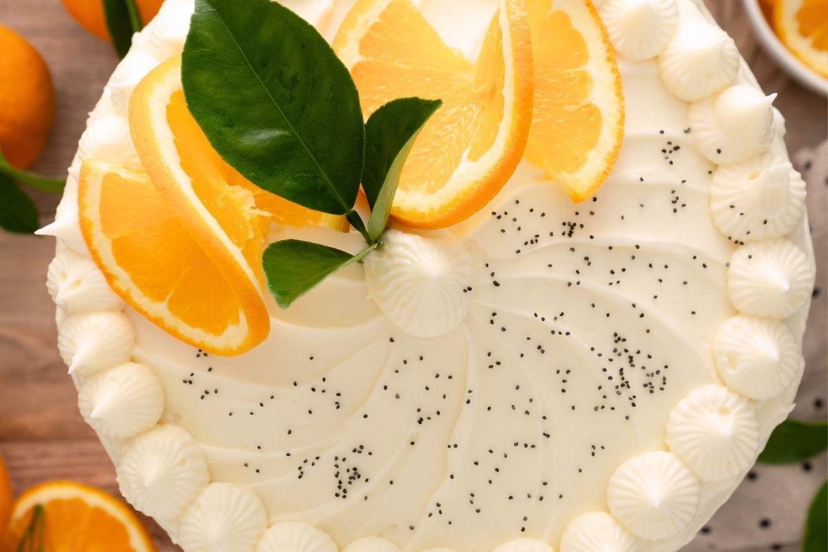 Overhead view of finished cake with orange slices, leaves, and poppy seeds.