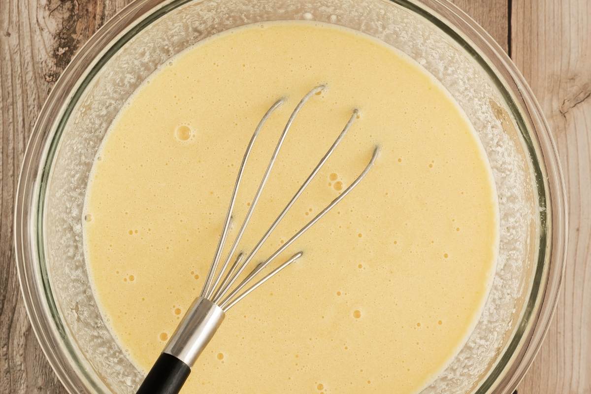 Yellow wet ingredients mixture in a glass bowl with a whisk.