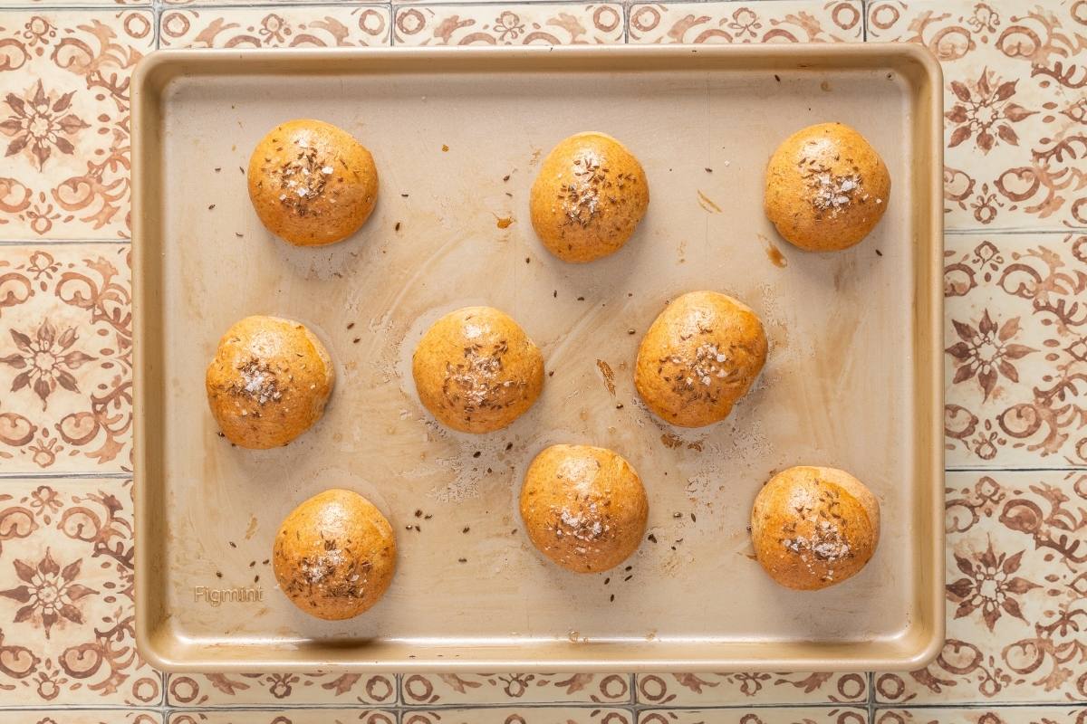 Golden-brown baked rye dinner rolls on a baking sheet, seen from above.